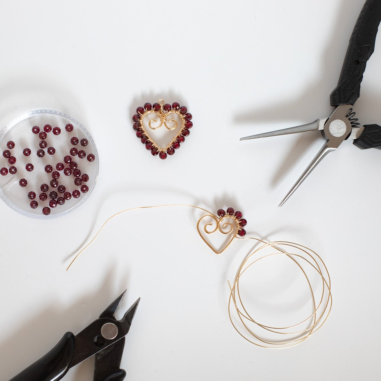 Jewelry-making tools and materials including pliers, beads, and earring components on a white surface.