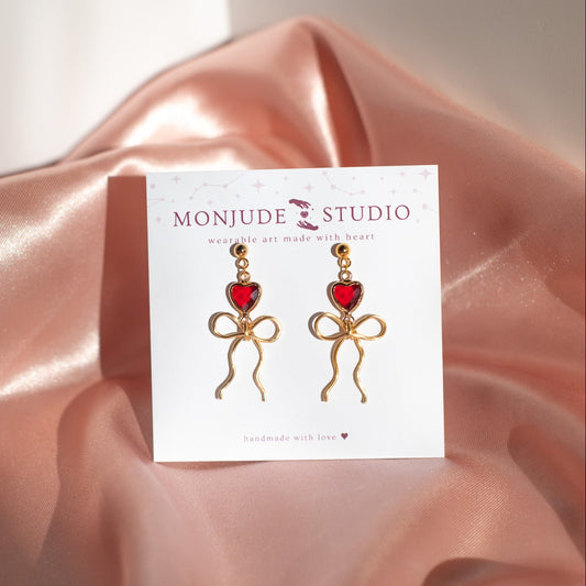 Earrings on a Monjude Studio card with pink fabric background