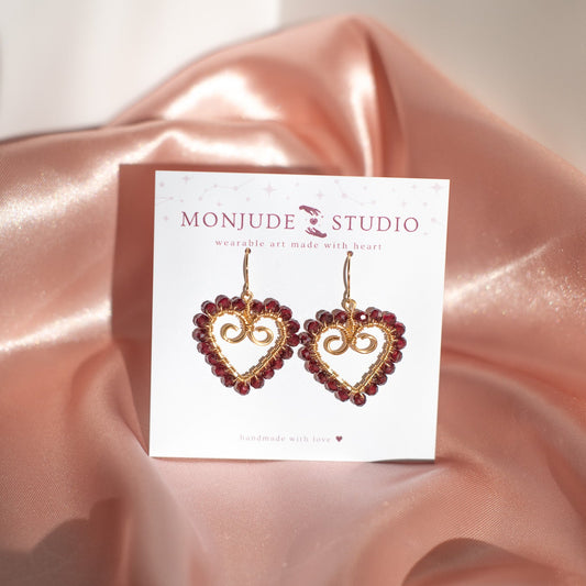 Heart-shaped earrings on a Monjude Studio card with pink satin fabric